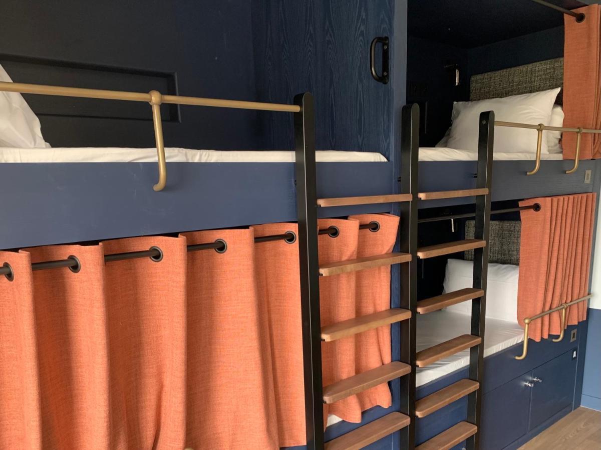 The People - Paris Nation Hostel Exterior photo The photo shows a compact sleeping area featuring bunk beds. The bunk beds have a modern design with a dark blue wall behind them. The top bunk is adorned with a white mattress and pillow, and there are orange curtains hanging at the front of both bu