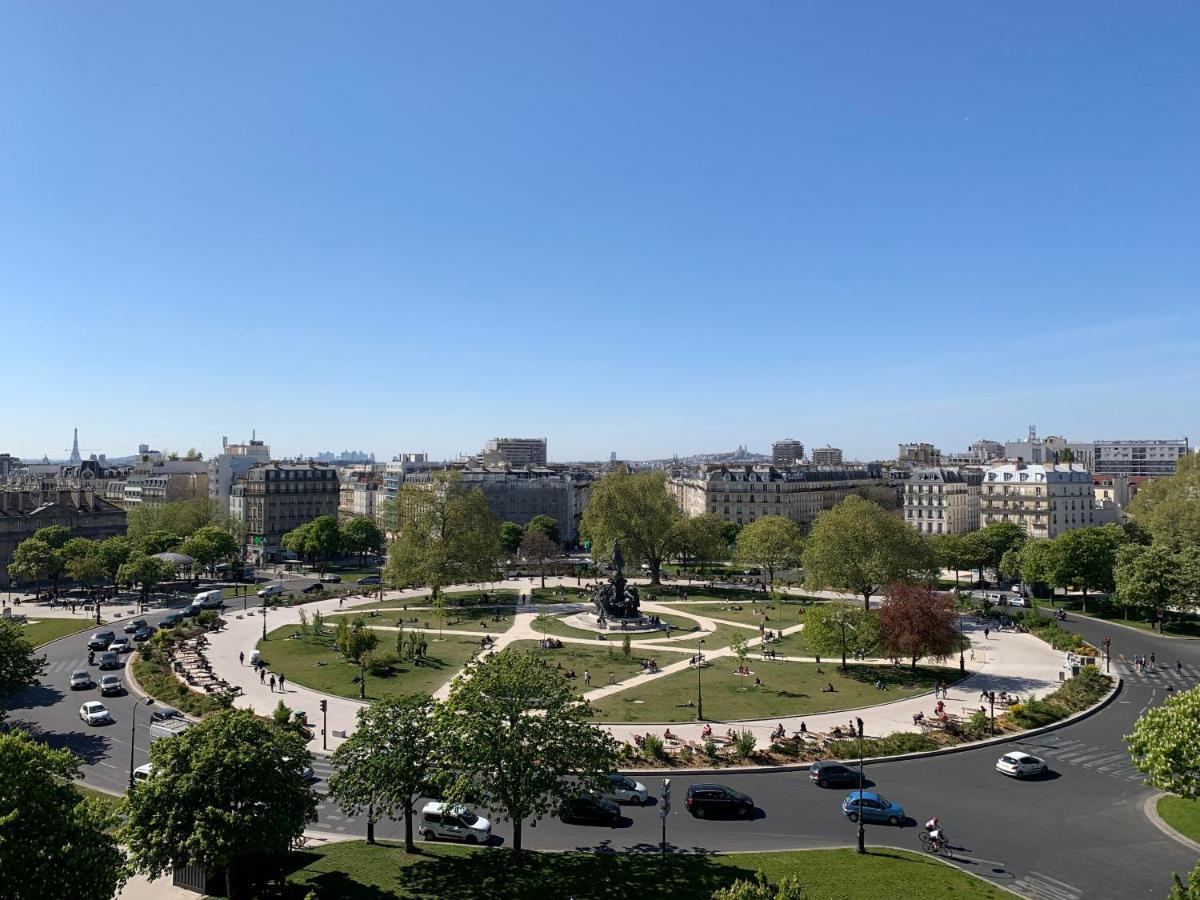 The People - Paris Nation Hostel Exterior photo The photo shows a scenic view of a circular plaza surrounded by greenery and trees. In the center of the plaza, there's a monument or statue. The area appears to be lively, with several vehicles circulating around the roundabout and people possibly e