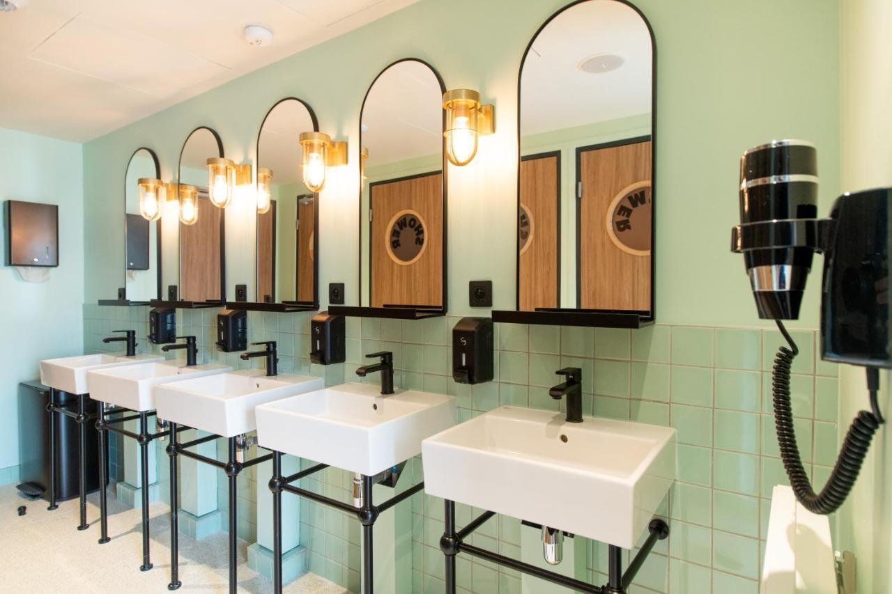 The People - Paris Nation Hostel Exterior photo The photo shows a modern restroom with several white sinks arranged in a row. Each sink is mounted on a black metal frame and has a sleek black faucet. Above the sinks, there are large rectangular mirrors with rounded tops, framed in black. The walls