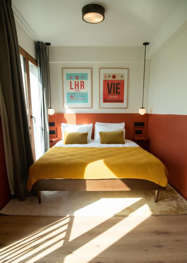 The People - Paris Nation Hostel Exterior photo The photo shows a stylish hotel room featuring a comfortable double bed with white bedding and two mustard-yellow pillows. Above the bed, there are two framed posters, one with "LHR" and the other with "VIE," suggesting a travel theme. The walls are 