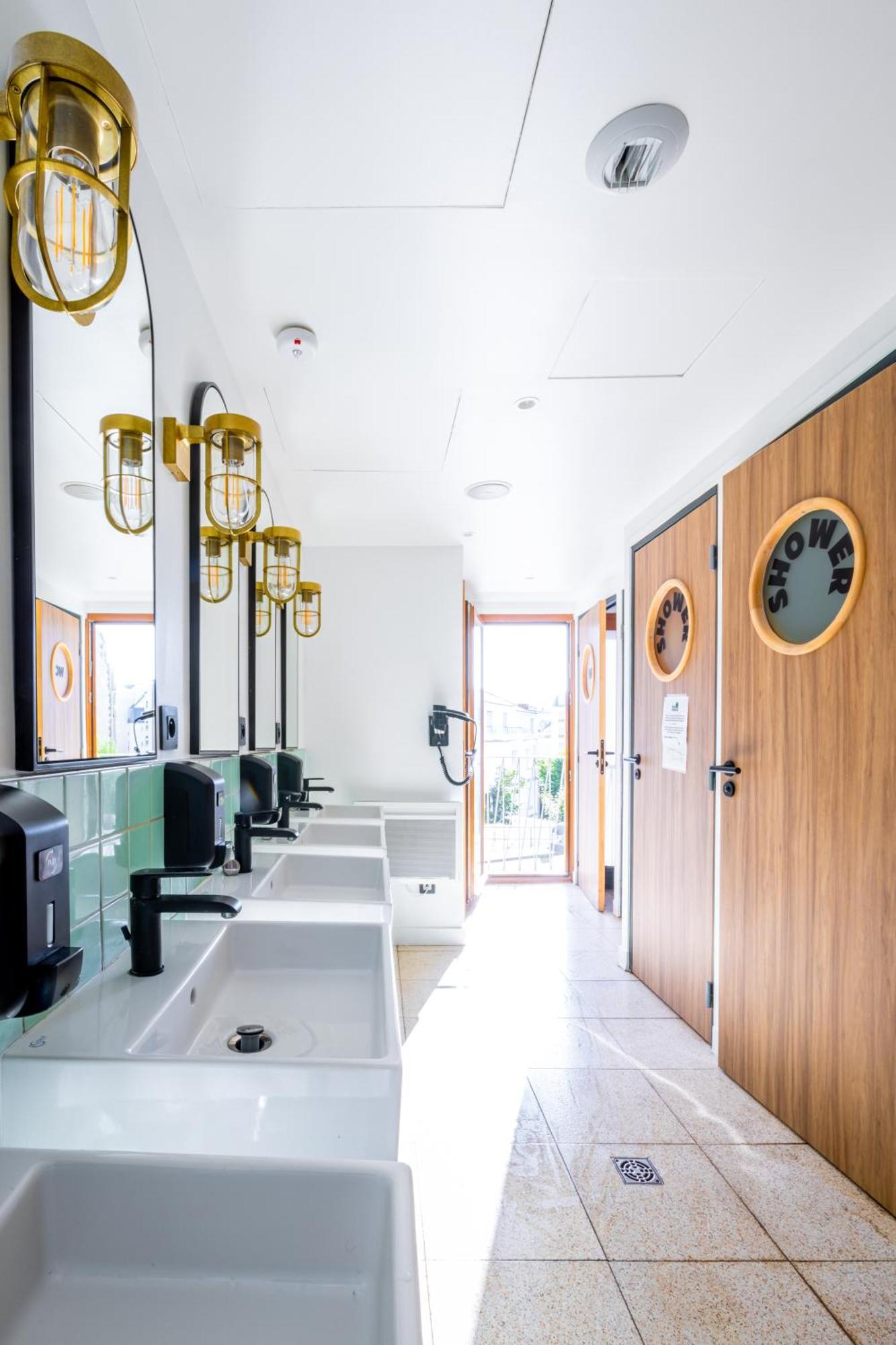 The People - Paris Nation Hostel Exterior photo The photo shows a modern restroom environment. It features a row of sinks with stylish black faucets and hand dryers. Above the sinks, there are large mirrors and yellow pendant lights that add a warm touch. On the right side, there are two doors lab