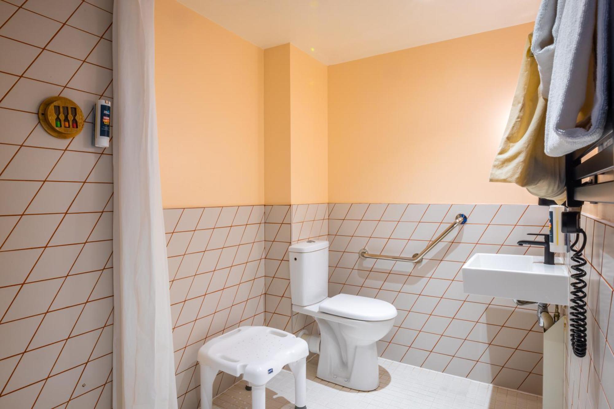 The People - Paris Nation Hostel Exterior photo The photo shows a bathroom with a simple and functional design. The walls are painted in a light orange color, while the lower half is tiled in a light beige pattern. In the bathroom, there is a white toilet and a small white stool. Next to the toile