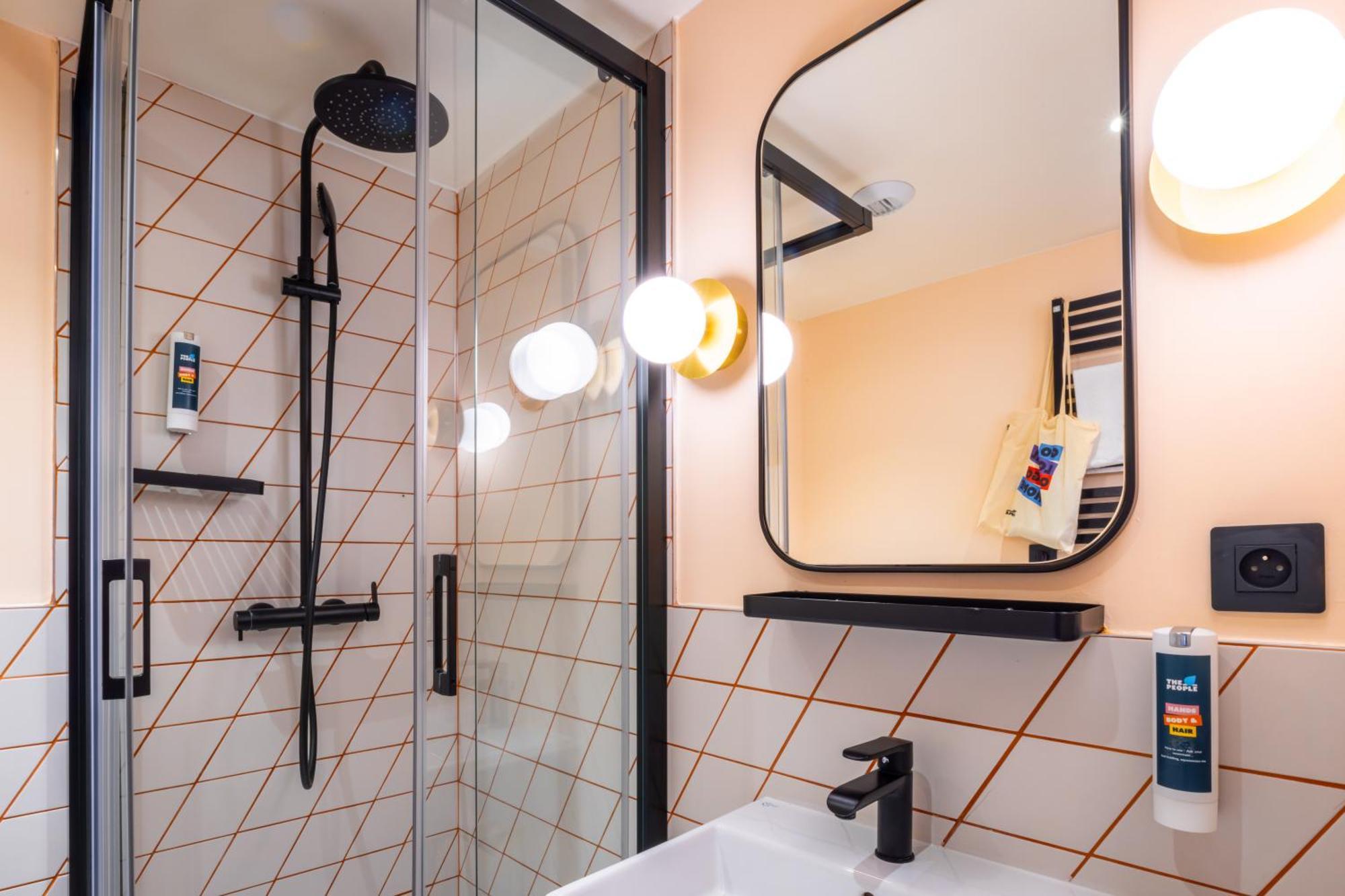 The People - Paris Nation Hostel Exterior photo The photo shows a modern bathroom. On the left, there is a glass shower enclosure with a rainfall showerhead and a minimalist design. The walls are tiled with a geometric pattern. To the right, there's a vanity area featuring a sleek, rectangular mir