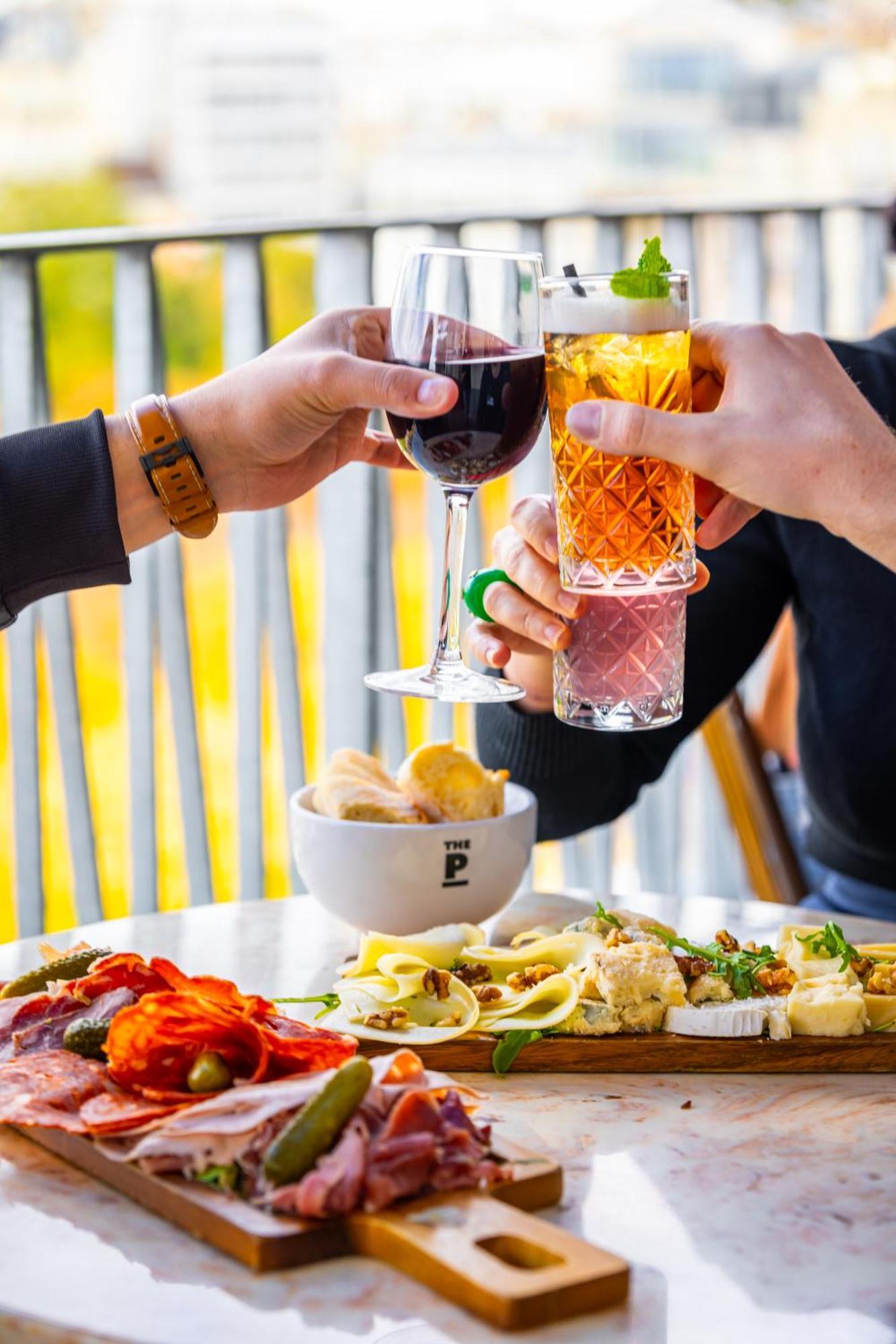 The People - Paris Nation Hostel Exterior photo The photo depicts a celebratory moment where several hands are raised, each holding a drink. There are two glasses of red wine and a colorful mixed drink. In the foreground, a spread of food is laid out on a table, featuring various dishes, including